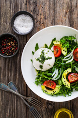 Burrata cheese with leafy greens, avocado and cherry tomatoes on wooden table
