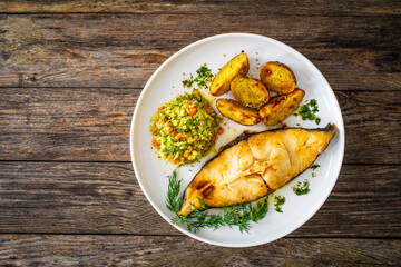 Fish dish - fried halibut with baked potatoes and cabbage salad on wooden table
