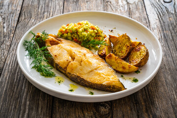 Fish dish - fried halibut with baked potatoes and cabbage salad on wooden table