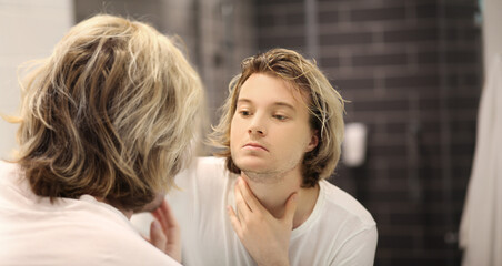 young man looking in the mirror,combing his hair,looking at problems on face.