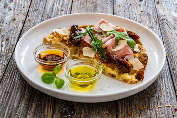 Pinsa Romana with mortadella, parmesan cheese and vegetables on wooden table
