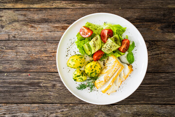 Fried halibut loin with boiled potatoes and fresh vegetables on wooden table
