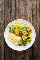 Fried halibut loin with boiled potatoes and fresh vegetables on wooden table

