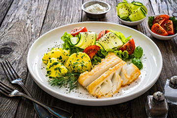 Fried halibut loin with boiled potatoes and fresh vegetables on wooden table
