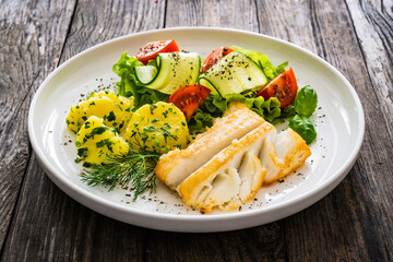 Fried halibut loin with boiled potatoes and fresh vegetables on wooden table
