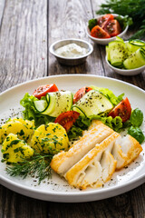 Fried halibut loin with boiled potatoes and fresh vegetables on wooden table
