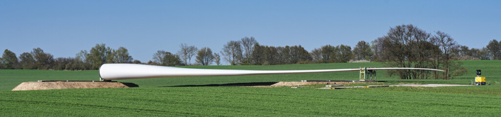 Panorama of a wind turbine blade on an agriculture field near the planned installation site,...