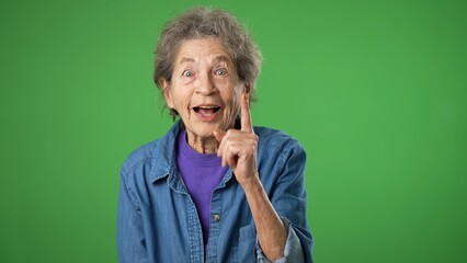 Portrait of thinking, smart puzzled pensive elderly senior old woman with wrinkled skin and grey hair looks around thinks with ideas raised finger thumbs up isolated on green screen background