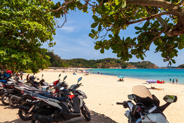 beautiful bright nai harn beach in thailand on phuket island with clear turquoise water in the sea, white sand, blue sky and motorbikes for rent.