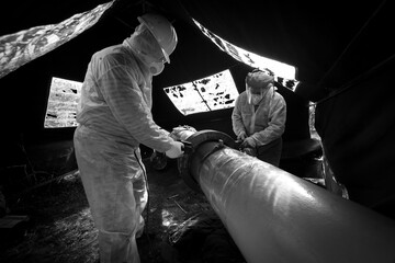 A worker in protective clothing performs a composite repair of a pipeline flange connection, black...