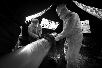 A worker in protective clothing performs a composite repair of a pipeline flange connection, black...