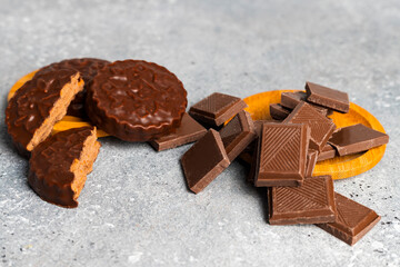Chocolate bar pieces and cookies lying in a round wooden stands against a gray spotted background.