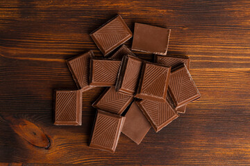 Chocolate bar pieces lying on a dark wooden table. flat lay, top view.