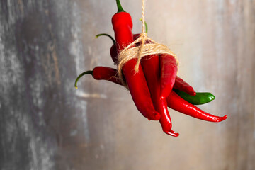 Red and green peppers tied together and hanging down on a rope but one is stand out.