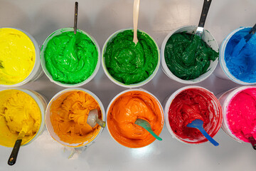 Top view, colorful fabric printing inks in white buckets..Stirring the ink for multicolored tee...
