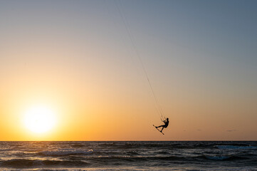 Black silhouette of a man on a wakeboard taking off over the Mediterranean Sea in Israel against the backdrop of sunset and horizon