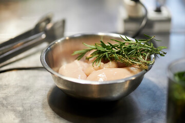 raw chicken fillet and rosemary branch in a metal bowl on the kitchen table, close-up. raw chicken meat and rosemary in a metal plate in the kitchen