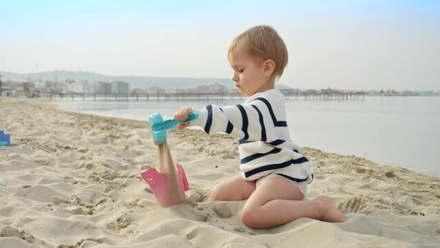 Cute little boy playing on the sandy beach and digging sand with a shovel. Joy, excitement, and freedom of a summer holiday with family