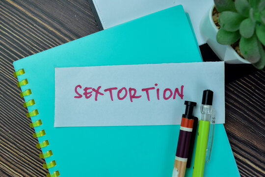 Concept of Sextortion write on sticky notes isolated on Wooden Table.
