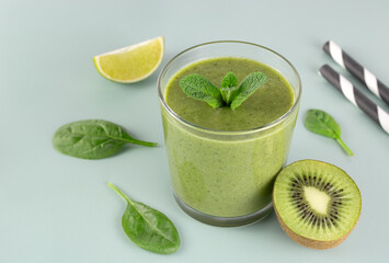 Green detox smoothie in glass on green background. Green smoothie with spinach, kiwi, banana, apple. 