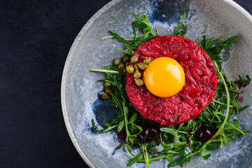 Modern style gourmet tartar raw from beef filet with egg, rucola and capers served as top view on a design plate with copy space right