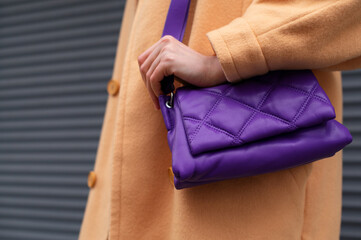 Street fashion elements: woman wearing trendy outfit with yellow coat, purple color padded faux leather shoulder bag. Copy, empty space for text