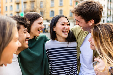 Multiracial young group of happy millennial people laughing together in city street. Diverse student friends hugging each other while talking and social gathering outdoors.