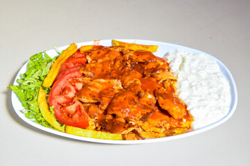 Turkish and Arabic Traditional Ramadan doner kebab with tasty tomato sauce and rice or turkish pilav in white plate on wood table background. ( Pilav ustu doner)