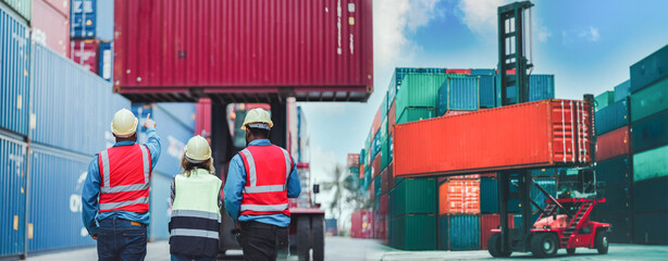 Industrial worker works with co-worker at overseas shipping container yard. Logistics supply chain...