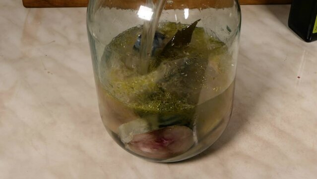 A man pours a mackerel in a glass jar cut into pieces with brine.