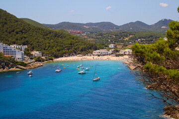 Obraz premium Cala Llonga bay on the southern side of Ibiza in the Balearic islands in the Mediterranean Sea - Cove with turquoise waters surrounded with pine covered hills