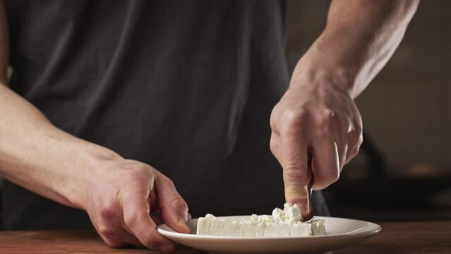 Male home chef making Bulgarian potato patties with white cheese. Crumbling feta cheese with a fork.