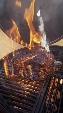 Traditional barbecue chianina bistecca alla Fiorentina beef steak grilled as close-up on a charcoal grill with fire and smoke – video and audio 