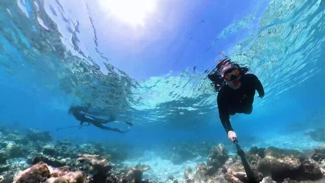 Man and woman are snorkeling in full body suit in tropical sea at the Maldives over corals with a rabbit hole effect in 360 degree video camera mode