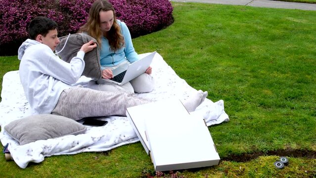 online learning outdoors boys girl sitting gadget outdoors picnic eating pizza learning lessons homework with a laptop in hands communication problem solving serious faces friends classmates