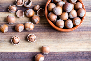 Hazelnuts in a shell and nutshells in ceramic bowl on rustic cutting board