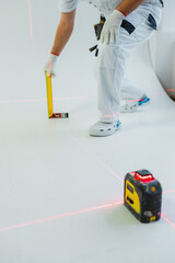 Builder in a white work uniform takes measurements with a laser ruler on a white background