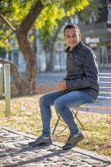 Young latin man sitting on a square bench.