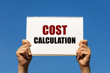 Cost calculation text on notebook paper held by 2 hands with isolated blue sky background. This message can be used as business concept about cost calculation.