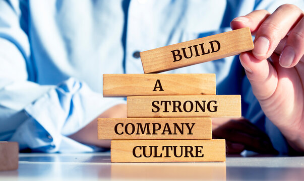 Close up on businessman holding a wooden block with a "Build a strong company culture" message