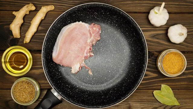 The meat is laid out on a frying pan with spices. The chef puts fresh juicy meat steaks on a marble pan. Spices for marinating pork and beef. Ginger, olive meat, cumin, garlic, mustard seeds, bay leaf
