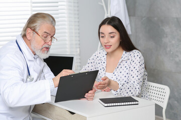 Senior doctor consulting patient at white table in clinic