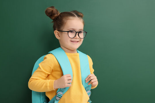 Happy little school child with backpack near chalkboard. Space for text