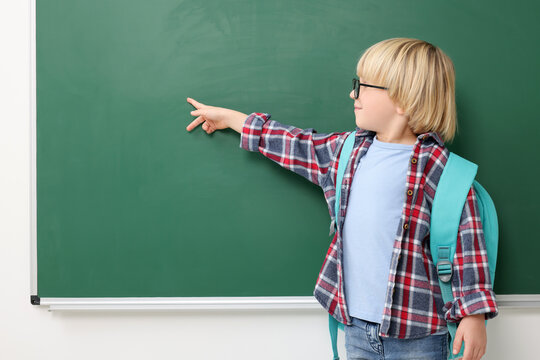 Little school child pointing at chalkboard. Space for text