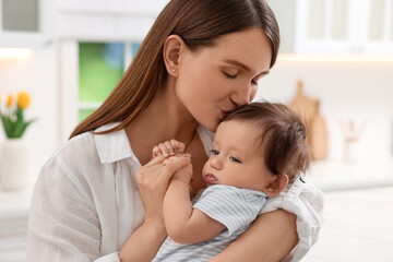 Happy mother kissing her little baby in kitchen
