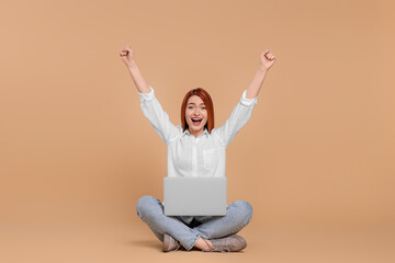 Happy young woman with laptop on beige background