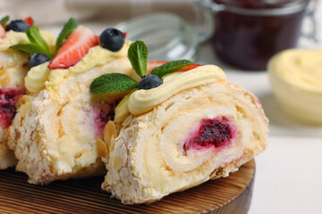 Pieces of tasty meringue roll with jam, cream, strawberry, blueberry and mint on table, closeup