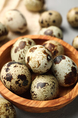 Obraz premium Wooden bowl and many speckled quail eggs on table, closeup