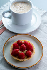 Breakfast with cup of black coffe and baked small tart with cream and fresh ripe red raspberry fruits