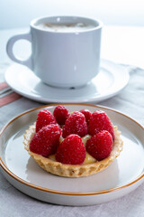Breakfast with cup of black coffe and baked small tart with cream and fresh ripe red raspberry fruits